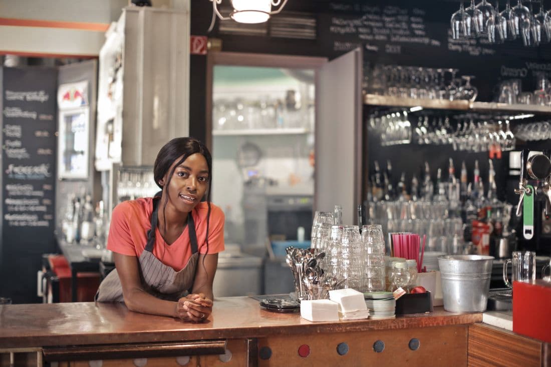 Une barmaid souriante accoudée au comptoir de son établissement