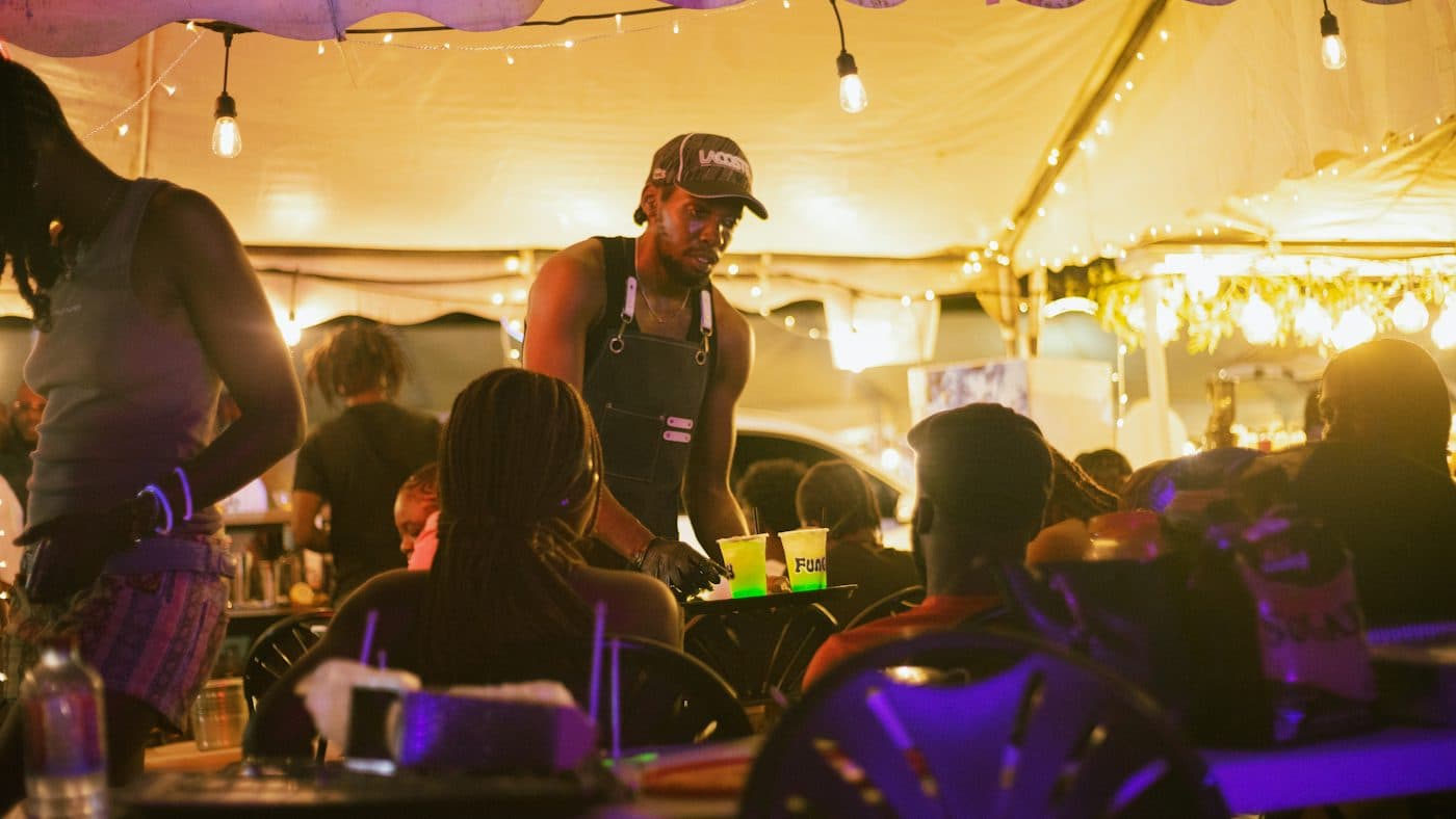 Un serveur passe entre des tables pleines un soir de service, sous des guirlandes lumineuses